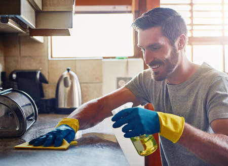 He never misses a spot. Cropped shot of a young man cleaning a kitchen surface at home.