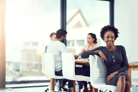 Im part of a great team. Cropped portrait of a young woman sitting in the office with her colleagues in the background.の写真素材