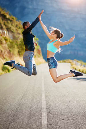 Theyre pumped up for fitness. Shot of a sporty young couple high fiving each other in midair outside.の写真素材