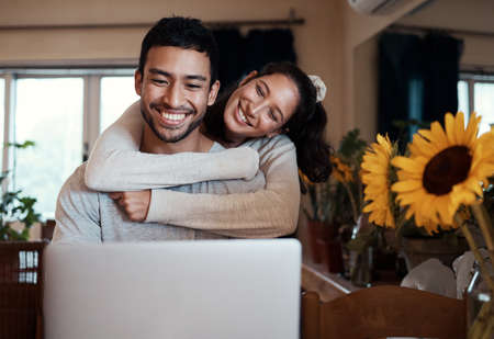 Shot of a man using his laptop while his girlfriend embraces him from behind.