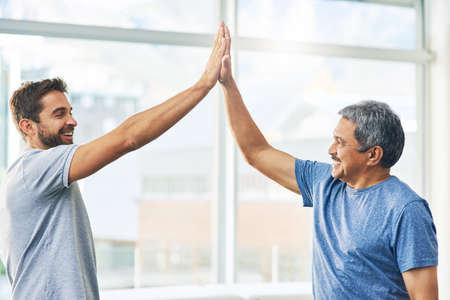Well done. Cropped shot of a young male physiotherapist and his senior patient high fiving after a great session.の写真素材