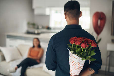 Ive got a surprise for you. Shot of a young man surprising his wife with flowers at home.の写真素材