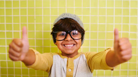 Approved by children. Shot of a cute little boy wearing glasses and a beanie showing thumbs up.の写真素材