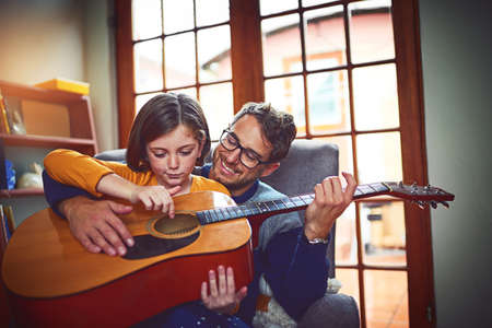 Theyre a father and daughter rockstar duo. Shot of a little girl playing the guitar with her father at home.の写真素材