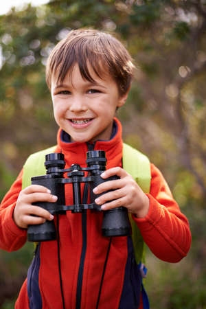 On the lookout for my next adventure. Portrait of a happy young boy out in the woods with a pair of binoculars.の写真素材