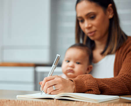 Notes are important to keep track of your responsibilities. Cropped shot of an attractive young woman working at home with her newborn baby sitting on her laptop.の写真素材