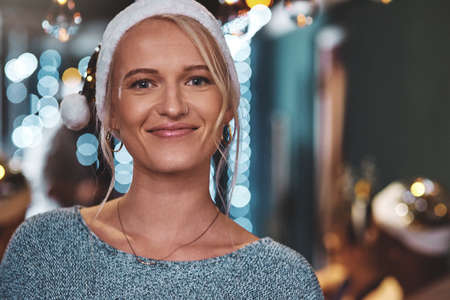 Im getting in touch with the christmas spirit. Portrait of a cheerful young woman wearing a festive hat at home during christmas time.の写真素材