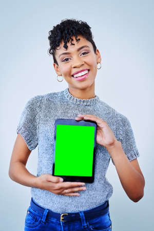 Read up about me on here. Portrait of an attractive young woman holding up a digital tablet against a blue background.の写真素材