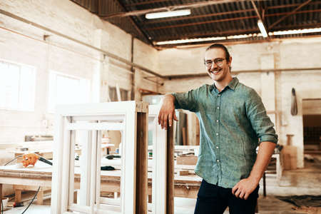 I just love creating pieces of art from wood. Portrait of a happy young carpenter posing inside a...