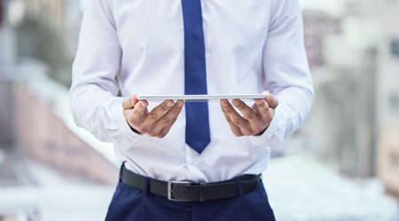 The handheld office. Cropped shot of an unrecognizable businessman holding his tablet while standing outside in the city.の写真素材