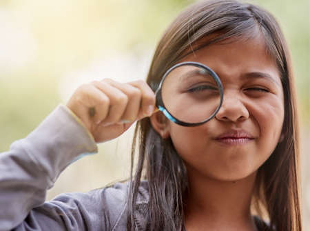 Shes on another one of her explorations. Portrait of a little girl looking through a magnifying glass.の写真素材