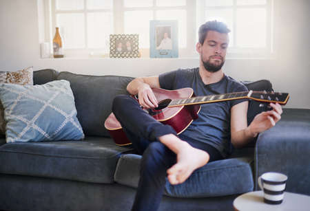 Hes developed a well-tuned musical ear. Cropped shot of a handsome young man playing a guitar at...