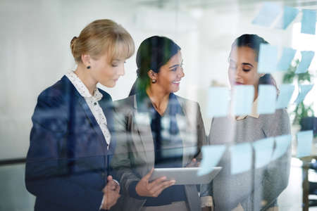 Work in progress. Cropped shot of a group of businesswomen working together on a digital tablet in an office.の写真素材