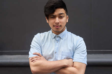Im not convinced. Portrait of a young man standing with his arms folded outside.