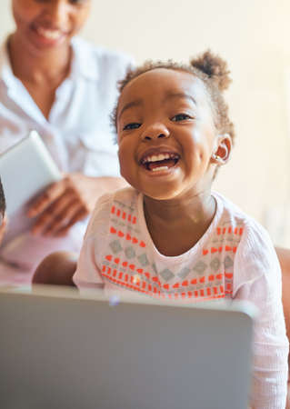 So much fun. Cropped portrait of an adorable little girl laughing while playing on a laptop at home.の写真素材
