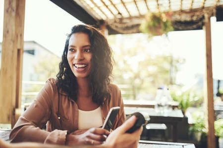 Leave your cash at home, pay with your phone. Shot of a young woman making a wireless payment in a...