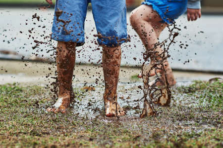 Be young, make a mess. Low angle shot of two unrecognizable children jumping around in mud outside during a rainy day.の写真素材