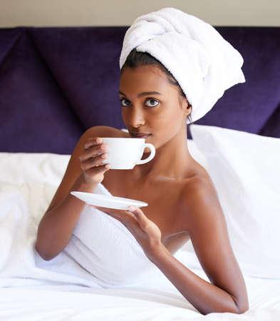 Its the perfect start to any holiday. Cropped portrait of an attractive young woman drinking tea while lying on her bed after a shower.の写真素材