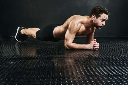 Core strength. Studio shot of a shirtless young man planking against a dark background.