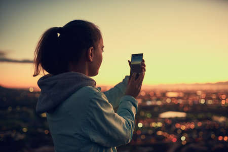 Theres always time for a photo. Rearview shot of a young woman sending a text message while standing...