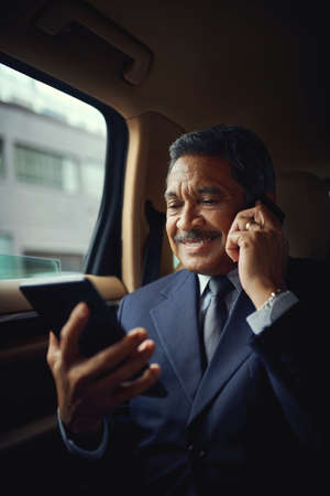 Tending to business matters on the move. Shot of a mature businessman using a phone and digital...