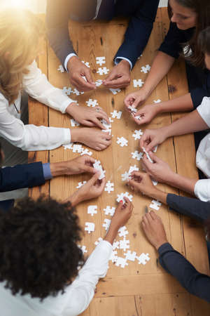 Finding solutions piece by piece. High angle shot of a group of businesspeople building a puzzle...