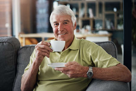 Afternoon tea always goes down well. Portrait of a senior man enjoying a beverage while relaxing on the sofa at home.の写真素材