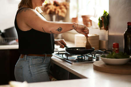 Stirring prevents sticking. Cropped shot of a woman preparing a meal at home.