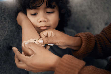 Mom is always there to make things better. Shot of a woman putting a plaster with a sad face drawn...