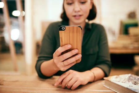 Theres nothing that I cant do with wood. Cropped shot of a female carpenter using her cellphone while sitting in her workshop.の写真素材