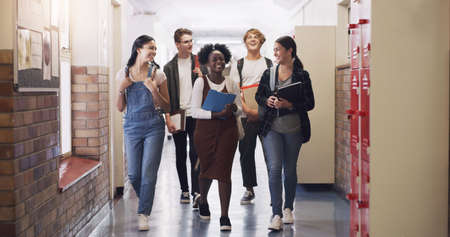 Keep learning, keep moving forward. Shot of a group of teenagers walking down the hall at high school.の写真素材