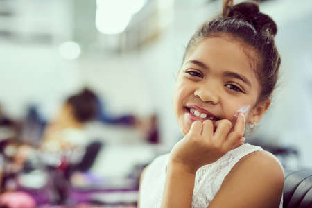 Youre never too young to look after your skin. Portrait of a cute little girl applying moisturizer to her face while sitting in a dressing room.の写真素材