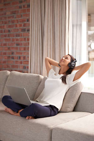 Relaxed tunes to match my mood. Shot of an attractive young woman listening to music on her laptop at home.の写真素材