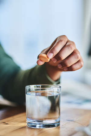 This will do the trick. Shot of an unrecognizable person putting a dissolvable tablet in a glass of water while being seated at a desk in the office.の写真素材