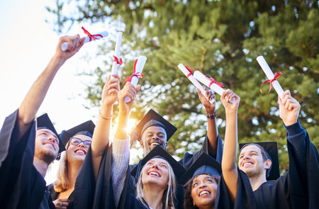 Our hard work paid off. Shot of a group of graduates holding their diplomas up in the air.の写真素材