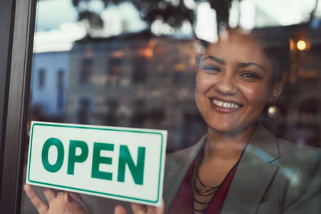 Shes eager to welcome all her customers. Portrait of a young business owner hanging up an open sign...