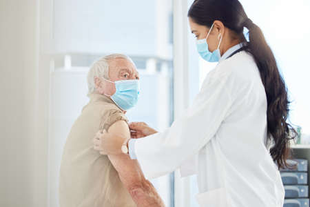 Itll be over before you know it. Shot of a doctor wearing a face mask and preparing her senior patient for a Covid vaccine in her clinic.の写真素材