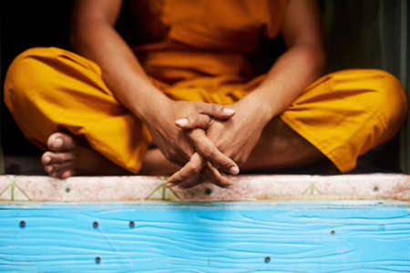 Living life simply. Shot of an unidentifiable buddhist monk sitting in the doorway of his home.の写真素材