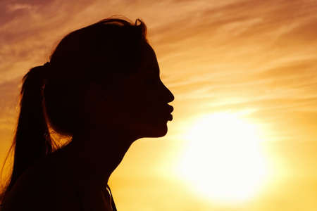 Closeup of a woman kissing the sun against beautiful sky. Profile view of a woman kissing the sun against beautiful sky.の写真素材