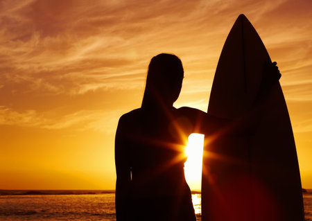 Silhouette of a woman holding a surfboard at sunset. Silhouette of a beautiful woman holding a surfboard at sunset.の写真素材