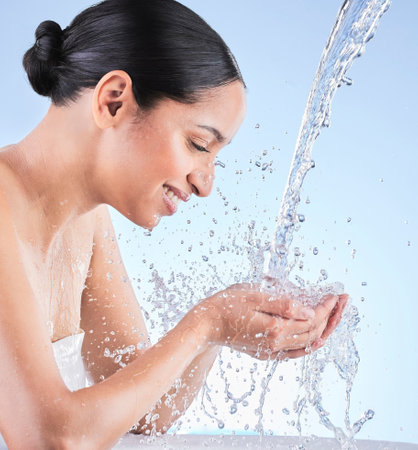 We all want that natural healthy glow. Shot of a young woman washing herself against a blue background.の写真素材