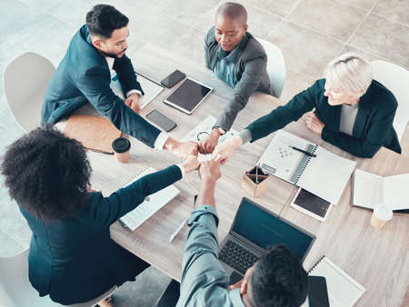 Weve got each other through all of this. High angle shot of a diverse group of businesspeople sitting in the office and forming a circle with their fists.の写真素材