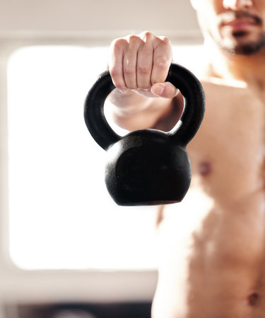 Hold this will you. Cropped shot of a young man working out with a kettle bell in a gym.の写真素材