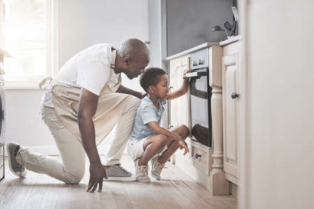 Its so much fun to mix all the ingredients. Shot of a father and son standing by the oven in the kitchen.の写真素材