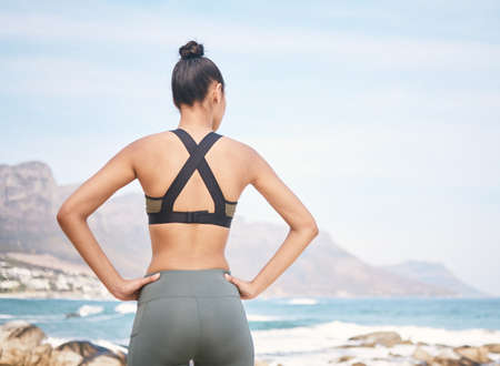 How can you not be motivated by this view. Rearview shot of an unrecognizable athletic young woman standing with her hands on her hips during a workout on the beach.の写真素材
