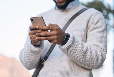 Stopping to text. Cropped shot of an unrecognizable businessman sending a text while standing outside in the city.の写真素材