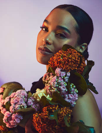 A beautiful arrangement. Studio portrait of an attractive young woman posing with a bouquet against a colourful background.の写真素材