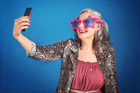Always capture the fun moments in life. Cropped hot of a funky and cheerful senior woman taking...
