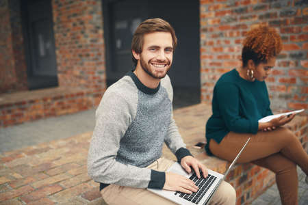 Getting some fresh air while studying. High angle shot of two young university students using a laptop to study on campus.の写真素材