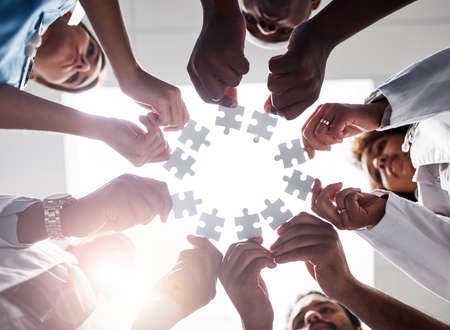 Everyone plays their part here. Low angle shot of a group of doctors forming a huddle while each holds a puzzle piece inside of a hospital.の写真素材